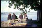 4 people sitting on a bench looking at the lake           